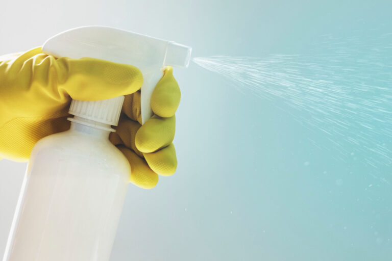 Rubber gloved hand holding white spray bottle with desinfectant